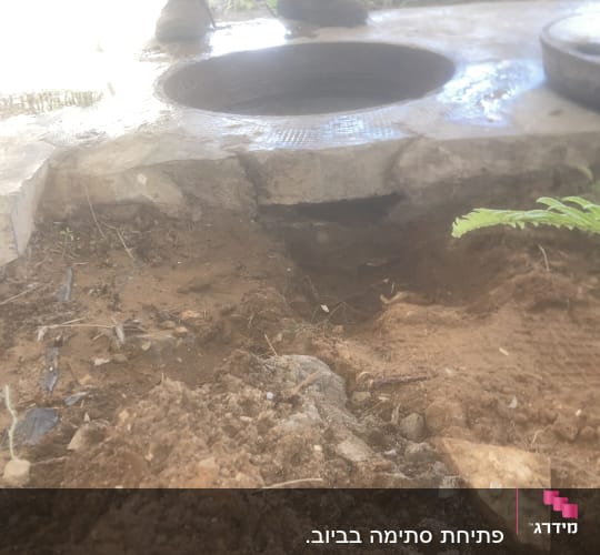 פתח ביוב עם אדמה מסביב, מגפיים נראות ברקע
